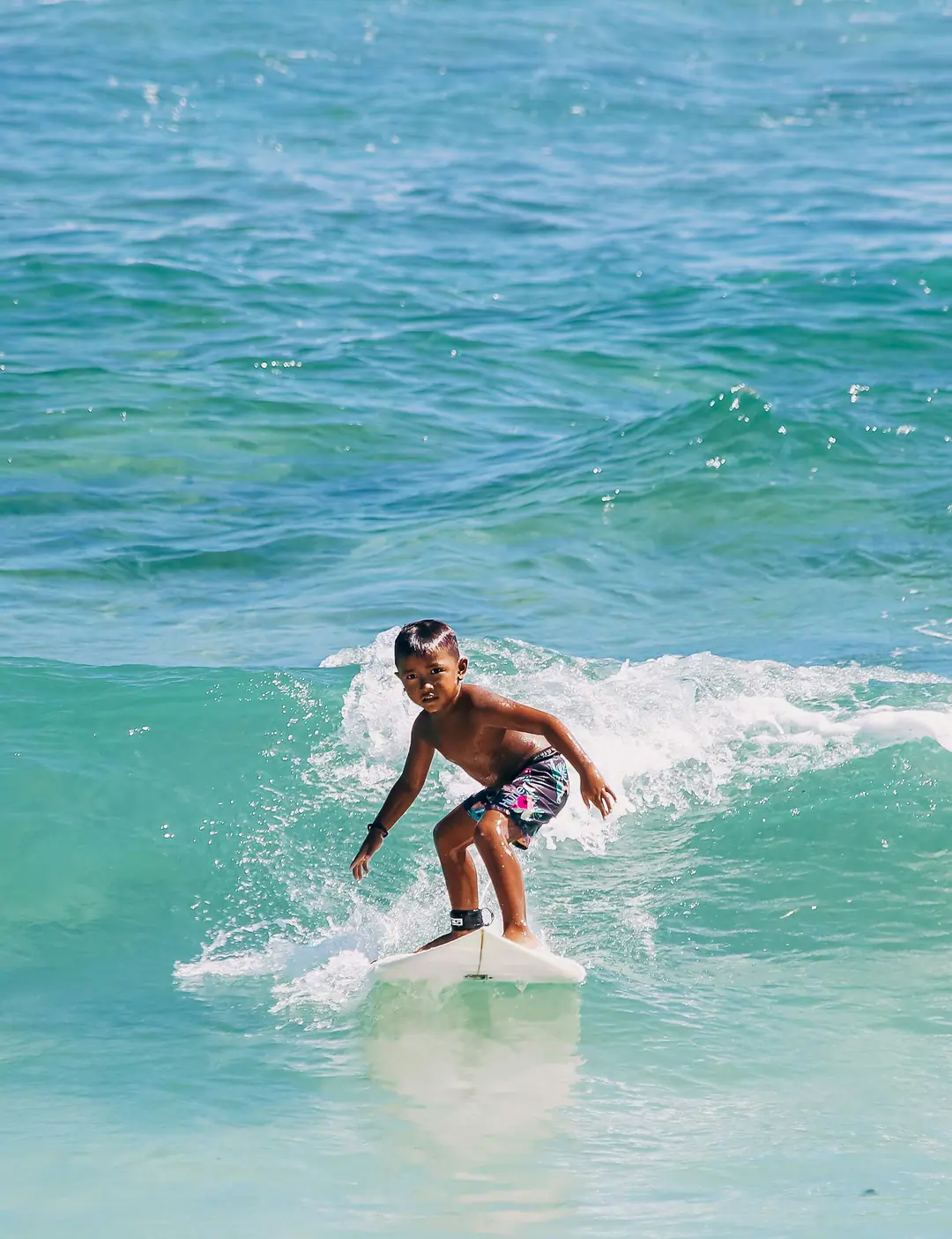 A young boy standing up on a surfboard in the whitewater