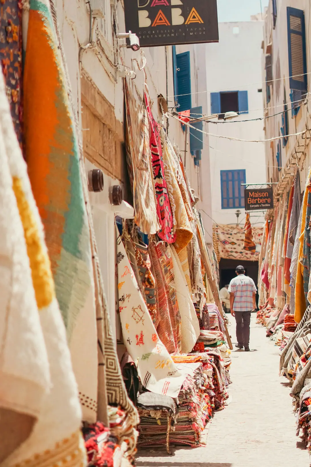 A narrow alley in Essaouira medina hung with colourful rugs and textiles