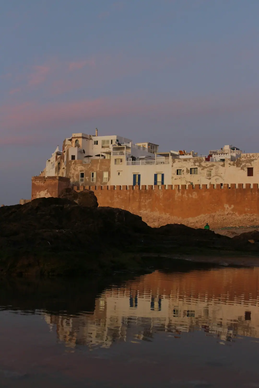 Essaouira's sea walls and houses reflected in the water at dusk
