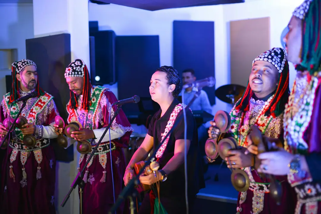 Des musiciens gnaoua en coiffe de cauris et tunique brodée, jouant avec un guitariste