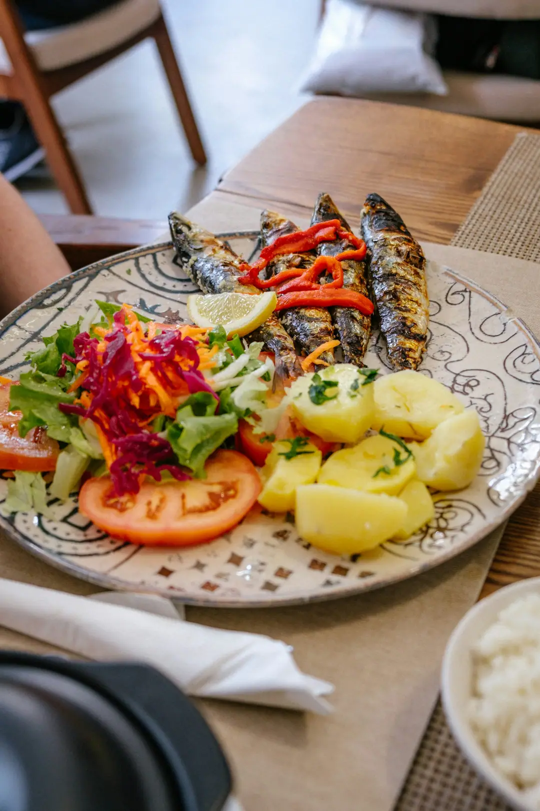 A plate of grilled sardines with salad and boiled potatoes