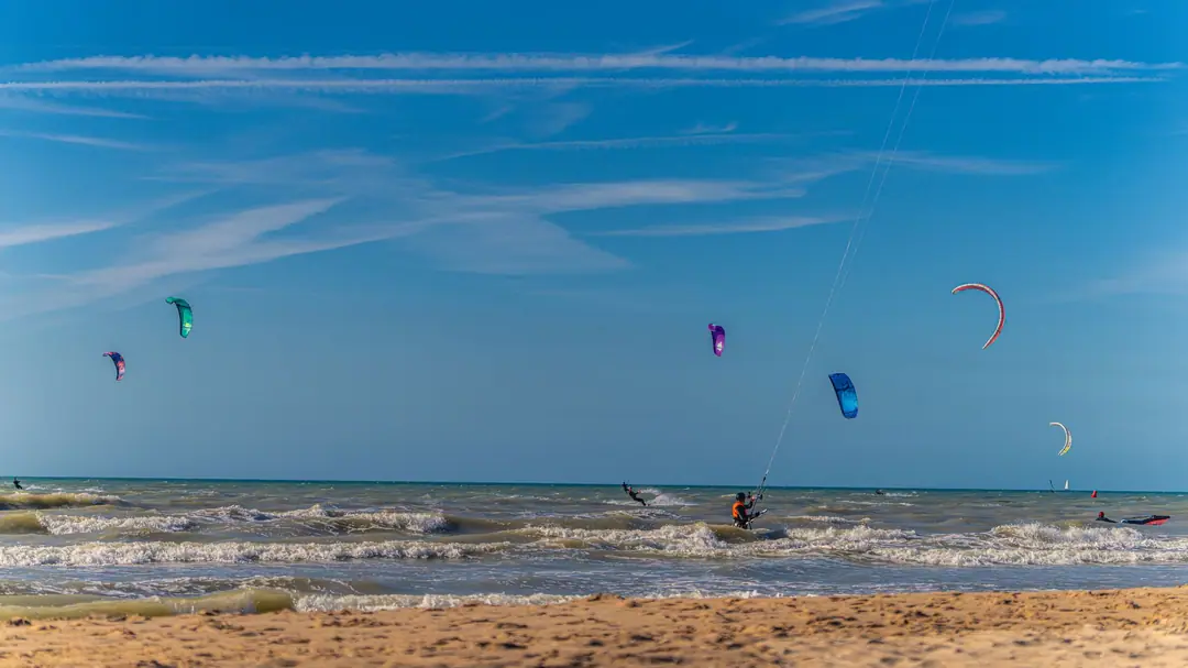 Kitesurfers and their colourful kites over the sea off a sandy beach