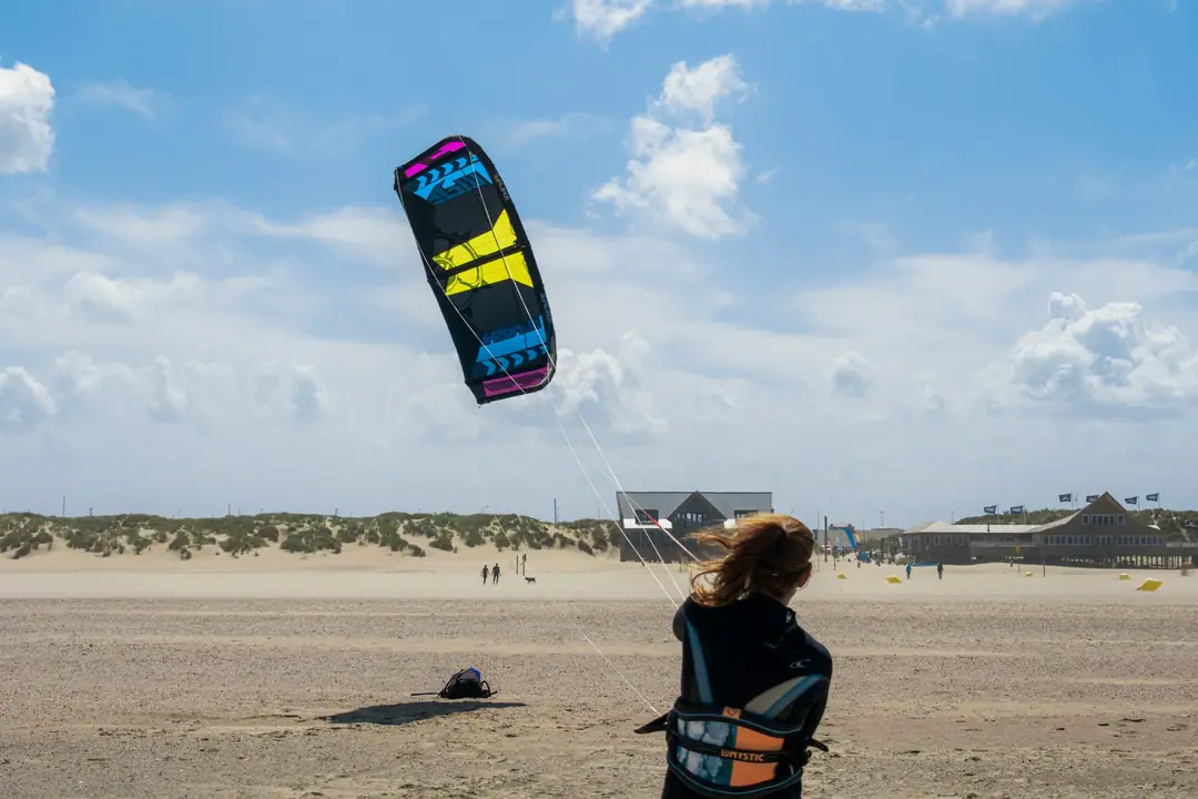 A kitesurfer in harness on a wide beach, flying a kite before heading out