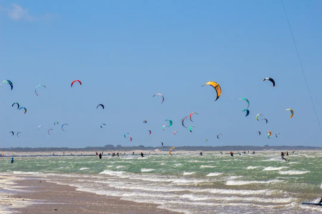 Dozens of kitesurfers and their kites over a windy bay