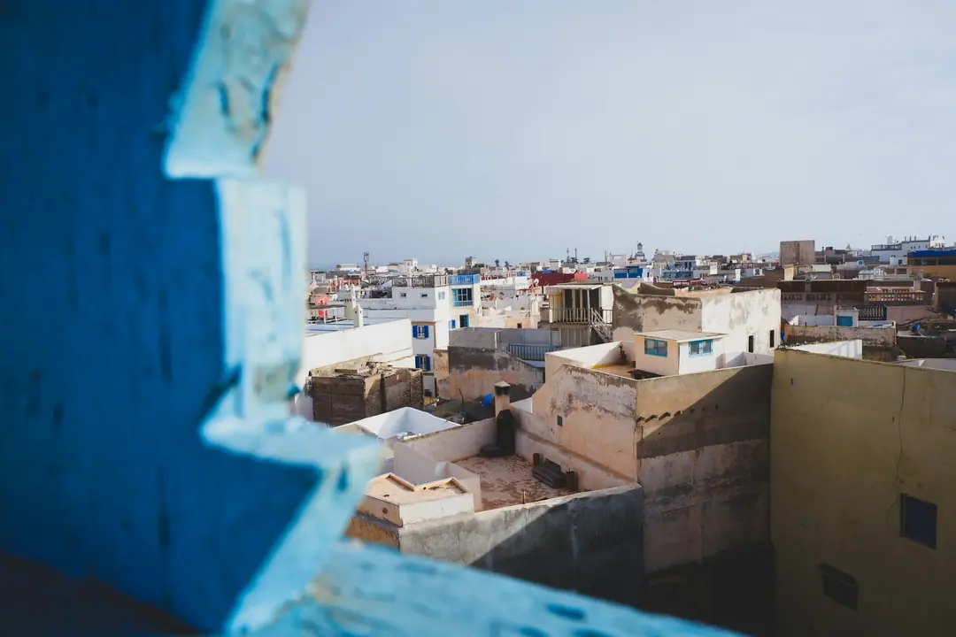 Whitewashed rooftops of a Moroccan medina framed by a blue window