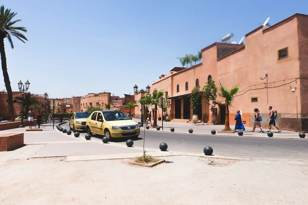 Beige petits taxis on a sunny Moroccan street lined with ochre walls and palms