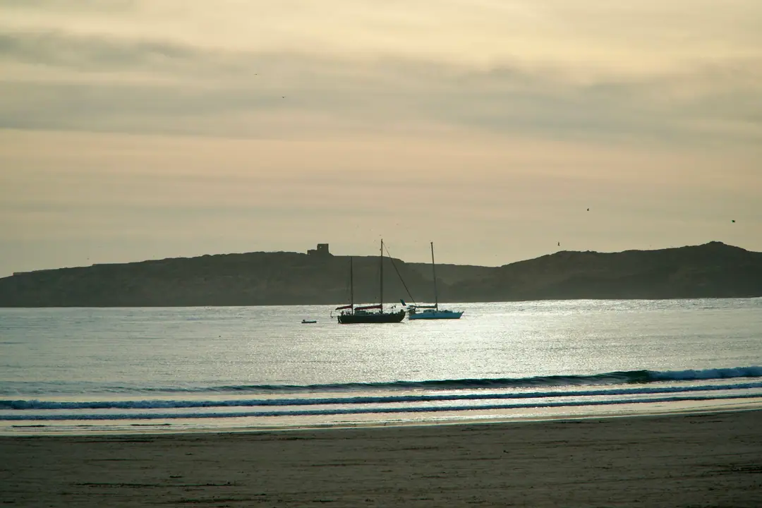 Deux voiliers au mouillage dans une baie calme au coucher du soleil, une île derrière