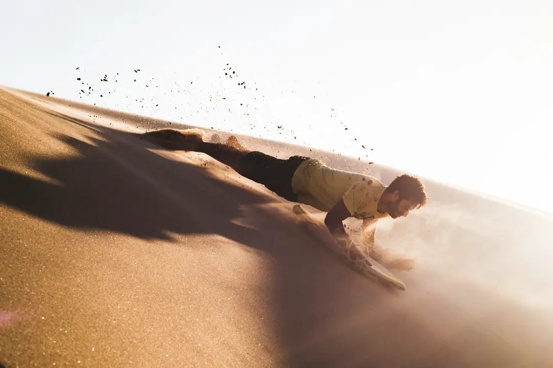 A sandboarder speeding down a golden dune in a spray of sand