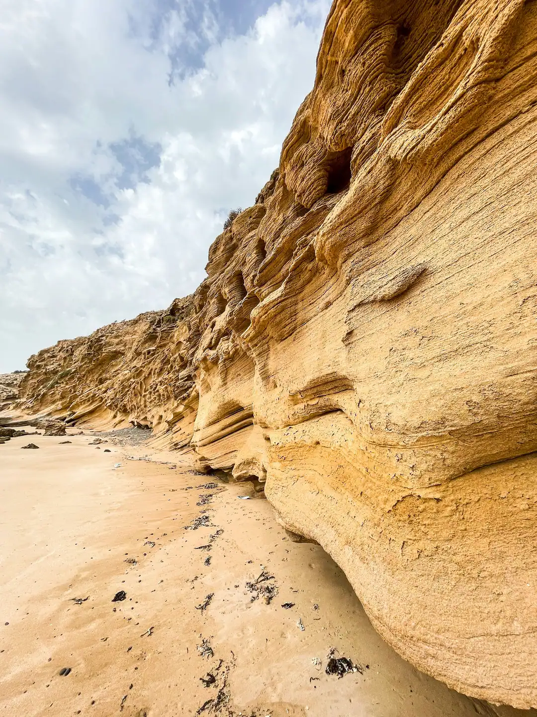 A sandy cove beneath tall, weathered sandstone cliffs